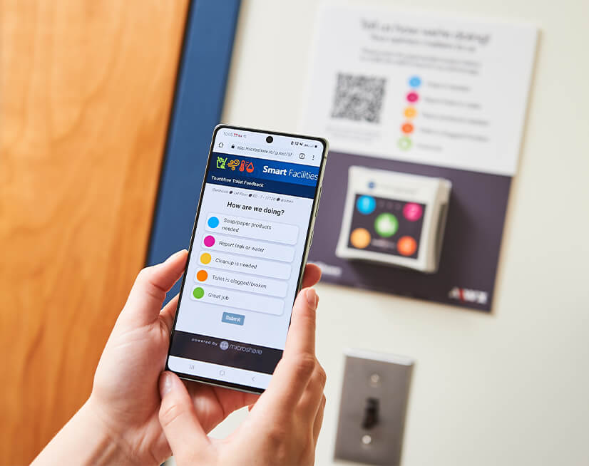A person using the AIWX Connect app on their phone to rate worker performance and report facilities issues.